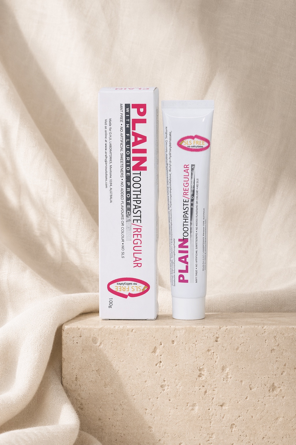 Plain Toothpaste carton and tube on a travertine plinth with draped cream linen fabric
